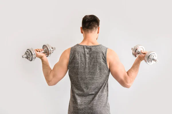 Sporty young man with dumbbells on light background — Stock Photo, Image