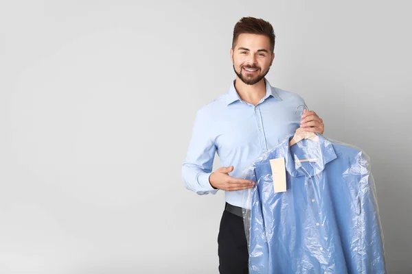 Male worker of modern dry-cleaner with clothes on light background — Stock Photo, Image