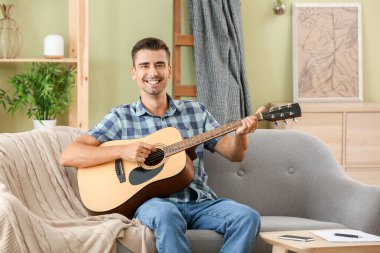 Yakışıklı adam evde gitar çalıyor.