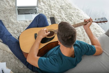 Yakışıklı adam evde gitar çalıyor.