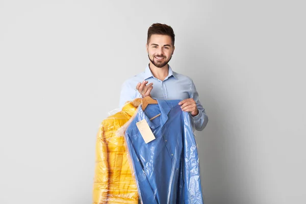 Male worker of modern dry-cleaner with clothes on light background — Stock Photo, Image