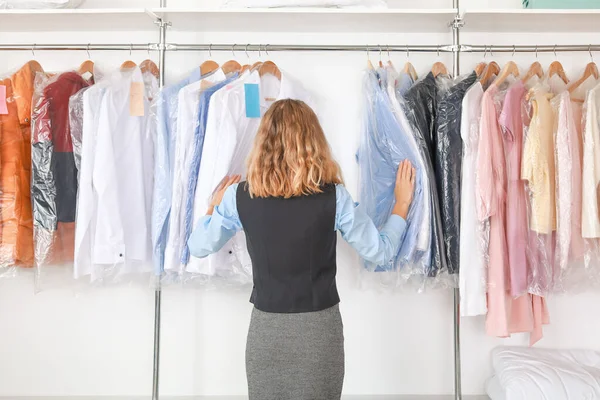 Jonge vrouwelijke werkster in de buurt van rek met kleren bij de stomerij — Stockfoto