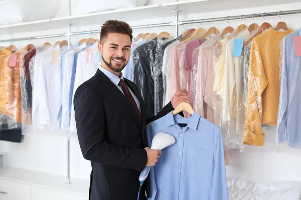 Jonge mannelijke werknemer stomende kleren bij de stomerij — Stockfoto