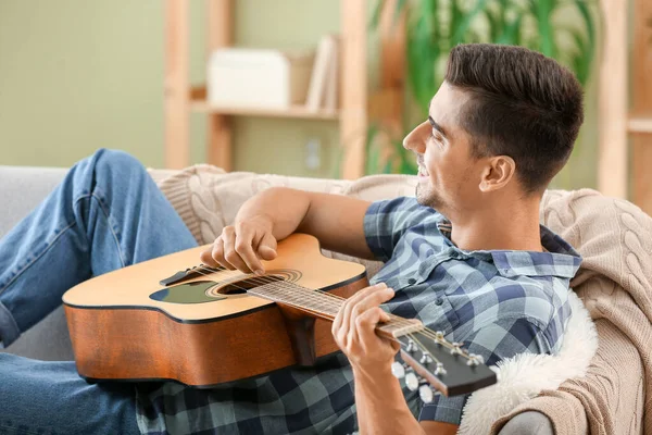 Yakışıklı adam evde gitar çalıyor.