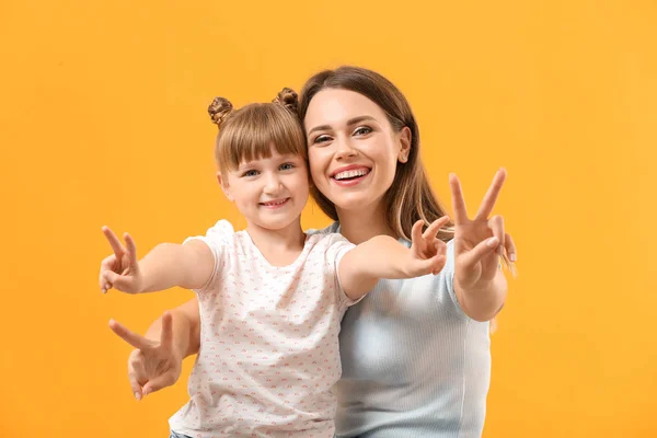 Portrait of happy mother and daughter showing victory gesture on color background — Stock Photo, Image