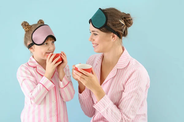 Portrait of happy mother and daughter in pajamas and with sleep masks drinking tea on color background — Stock Photo, Image