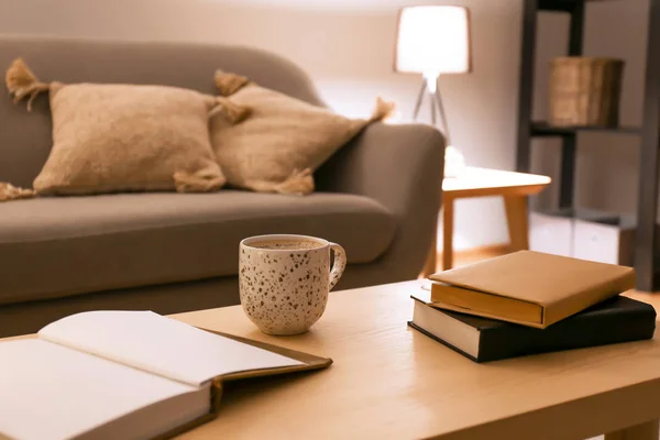 Books with cup of coffee on table in room at night — Stock Photo, Image