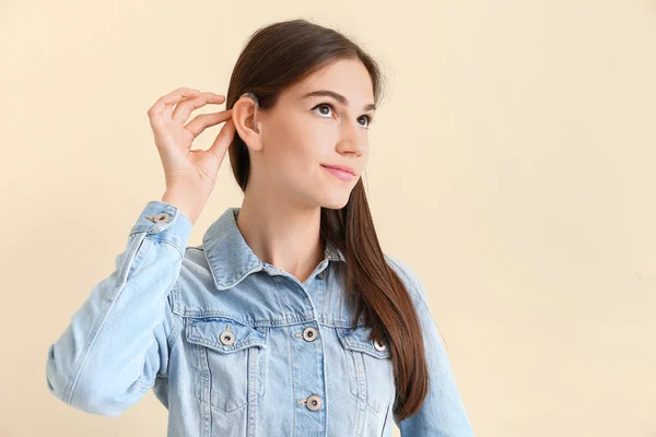 Young woman with hearing aid on color background — Stock Photo, Image