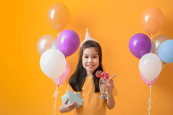 Petite fille avec des ballons d'air anniversaire, cadeau et bonbons sur fond de couleur — Photo