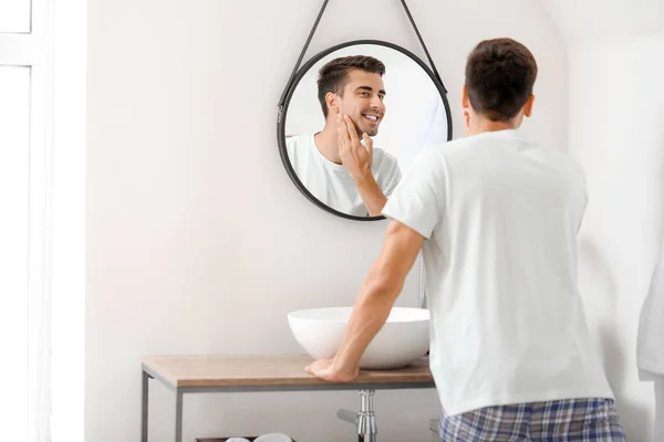 Schöner junger Mann, der nach der Rasur zu Hause in den Spiegel schaut — Stockfoto