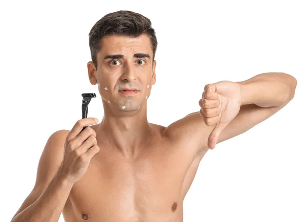 Unzufriedener junger Mann mit Rasiermesser zeigt Daumen nach unten auf weißem Hintergrund — Stockfoto