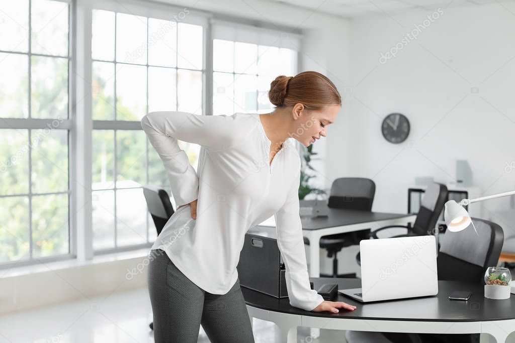 Young woman suffering from back pain in office