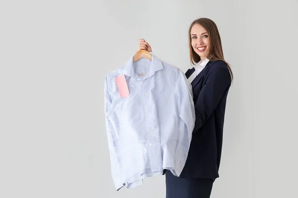 Vrouwelijke werkster van moderne stomerij met kleding op lichte achtergrond — Stockfoto