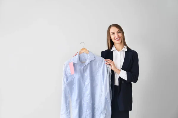 Female worker of modern dry-cleaner's with clothes on light background — Stock Photo, Image