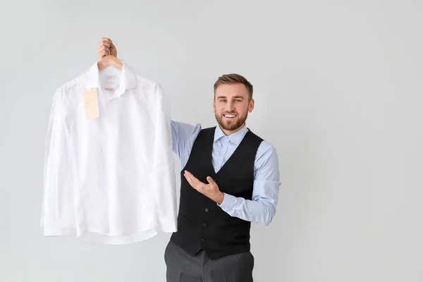 Mannelijke werknemer van moderne stomerij met kleding op lichte achtergrond — Stockfoto