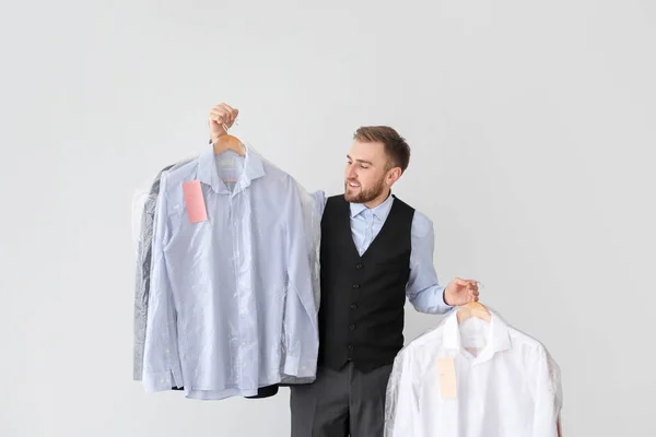 Trabalhador masculino da moderna lavandaria a seco com roupas em fundo claro — Fotografia de Stock