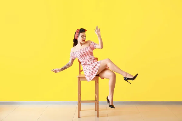 Portrait of beautiful tattooed pin-up woman sitting on chair against color wall — Stock Photo, Image