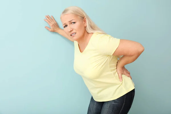 Mature woman suffering from back pain on color background — Stock Photo, Image