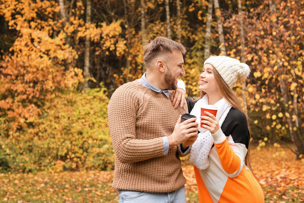 Loving young couple with cups of hot coffee in autumn park