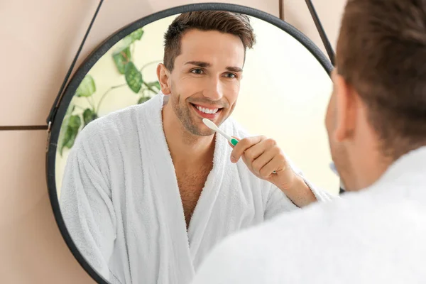 Handsome man cleaning teeth near mirror in bathroom — Stock Photo, Image