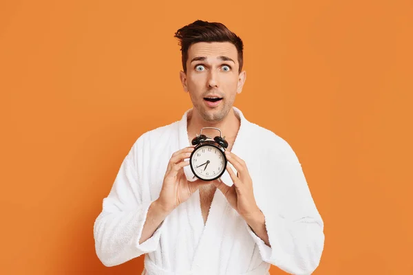 Surprised man in bathrobe and with alarm clock on color background — Stock Photo, Image