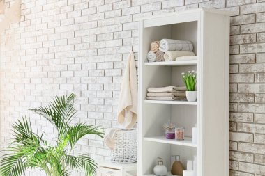 Havlu ve kozmetik ürünleri olan raf ünitesi banyoda tuğla duvarın yanında.
