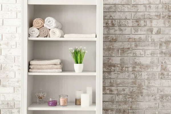 Shelf unit with towels and cosmetics near brick wall in bathroom — Stock Photo, Image