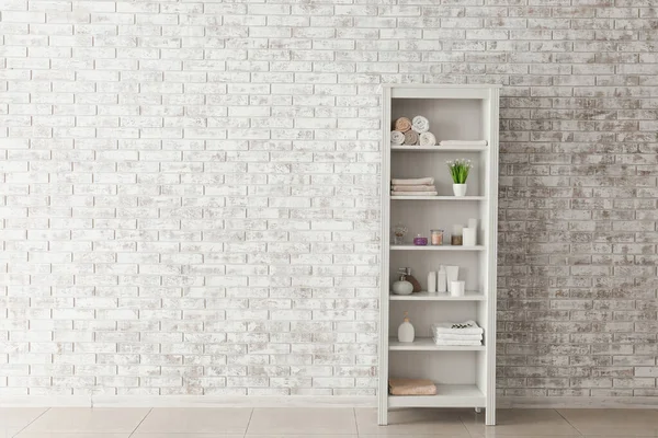 Shelf unit with towels and cosmetics near brick wall in bathroom — Stock Photo, Image
