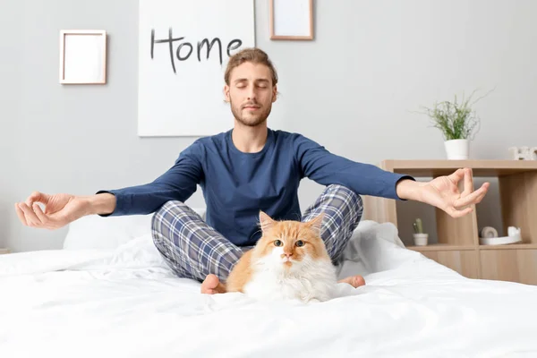 Young man with cute cat meditating in bedroom — Stock Photo, Image