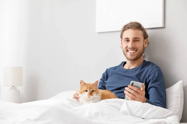 Man with mobile phone and his cute cat in bedroom — Stock Photo, Image
