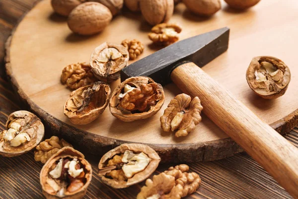 Доска с вкусными грецкими орехами и молотком на деревянном столе — стоковое фото
