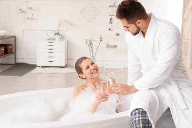 Mutlu genç çift banyoda şampanya içiyor.