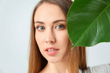 Açık arkaplanda tropikal yaprağı olan güzel genç bir kadın.