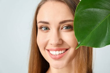 Açık arkaplanda tropikal yaprağı olan güzel genç bir kadın.