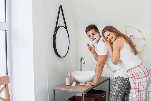 Morgon med vacker ung kvinna och hennes man med raklödder i ansiktet i badrummet — Stockfoto