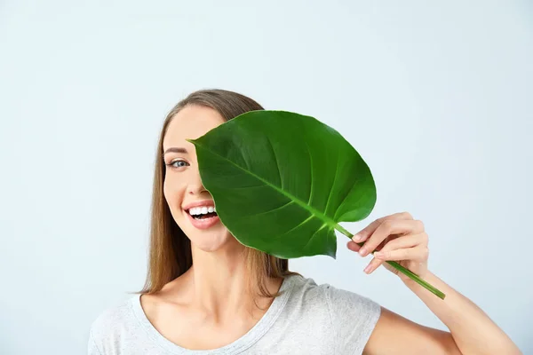 Mulher bonita com folha tropical no fundo claro — Fotografia de Stock