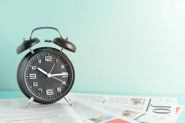 Alarm clock and newspapers on table near color wall — Stock Photo, Image