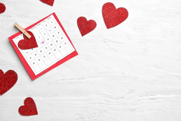 Calendar with marked date of Valentine's Day and red hearts on white wooden background — Stock Photo, Image