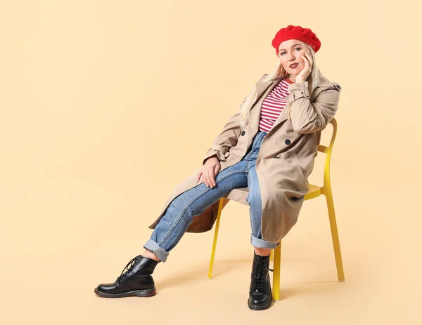 Renkli arka planda sandalyede oturan modaya uygun olgun bir kadın. — Stok fotoğraf