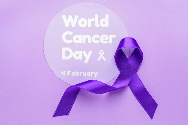 Papel com texto WORLD CANCER DAY e fita roxa sobre fundo de cor — Fotografia de Stock