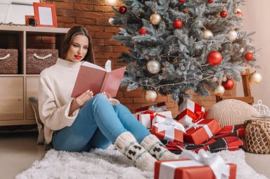 Güzel genç bir kadın Noel arifesinde evde kitap okuyor.