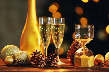 Noel dekorlu kum saati ve masadaki sönmüş ışıklara karşı şampanya.