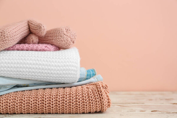 Set of warm winter clothes on table against color background