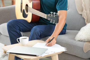 Evde gitar besteleyen yakışıklı bir adam.