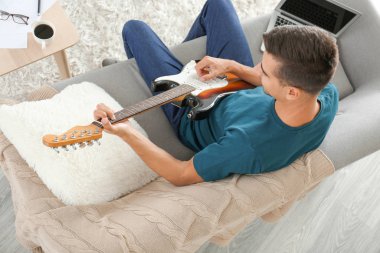 Yakışıklı adam evde gitar çalıyor.