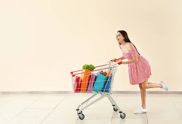 Young woman with shopping cart near light wall — Stock Photo, Image