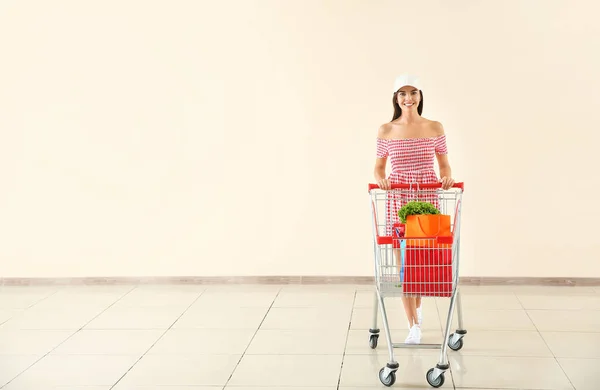 Jonge vrouw met winkelwagentje bij lichte muur — Stockfoto