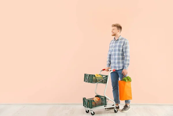 Young man with shopping cart near color wall — Stock Photo, Image