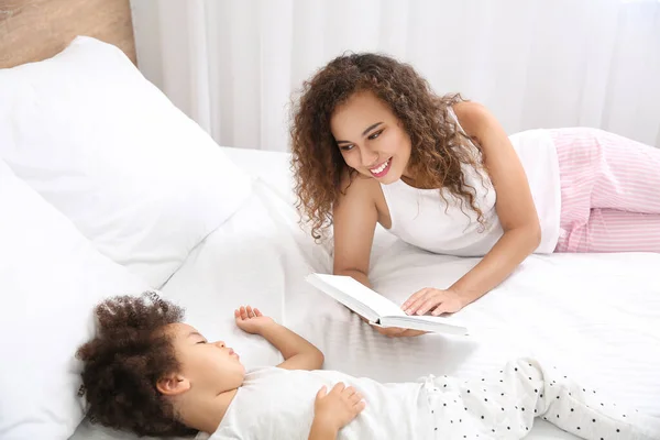 아프리카 계 미국인 어머니 침대에 자고 있는 딸을 위한 책을 읽고 있습니다. — 스톡 사진