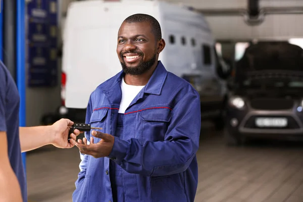 Cliente masculino dando a las llaves del coche mecánico afroamericano en el centro de servicio — Foto de Stock